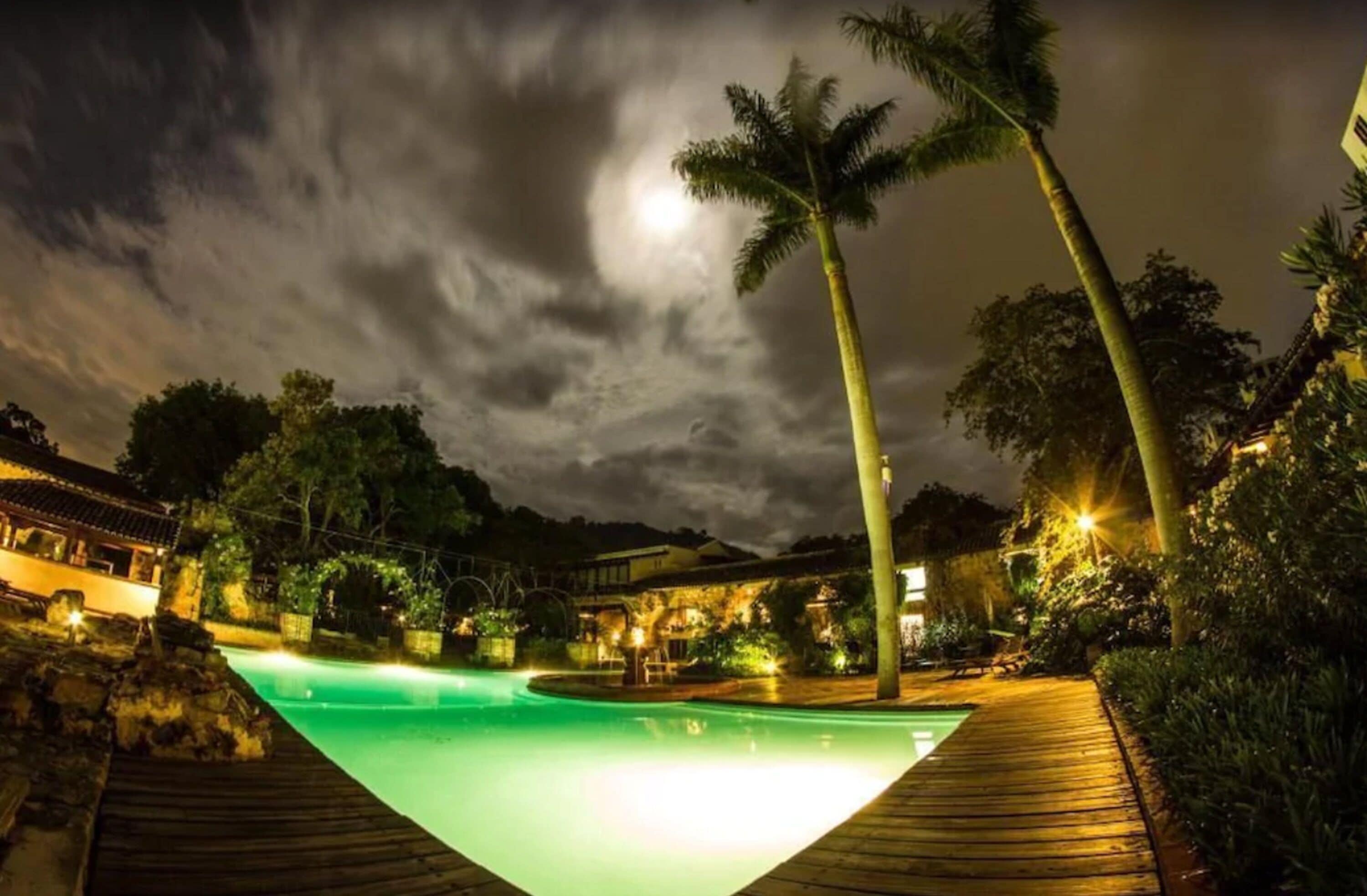 Een resort bij nacht met een zwembad, palmbomen en verlichte paden.