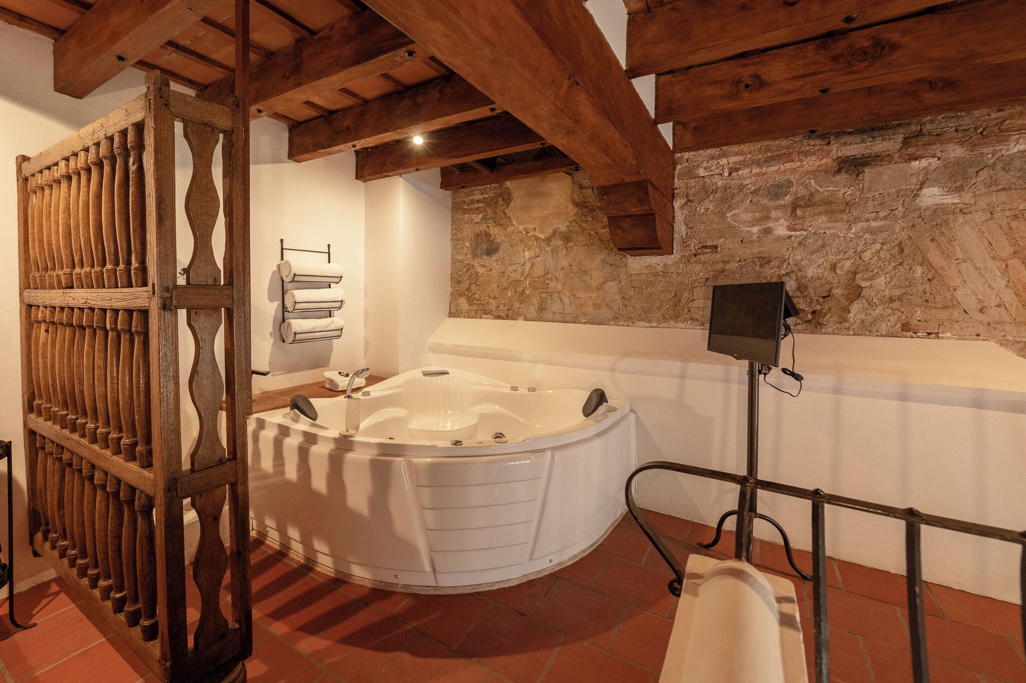 A bathroom with a large bathtub, wooden beams, stone wall, and a towel rack.
