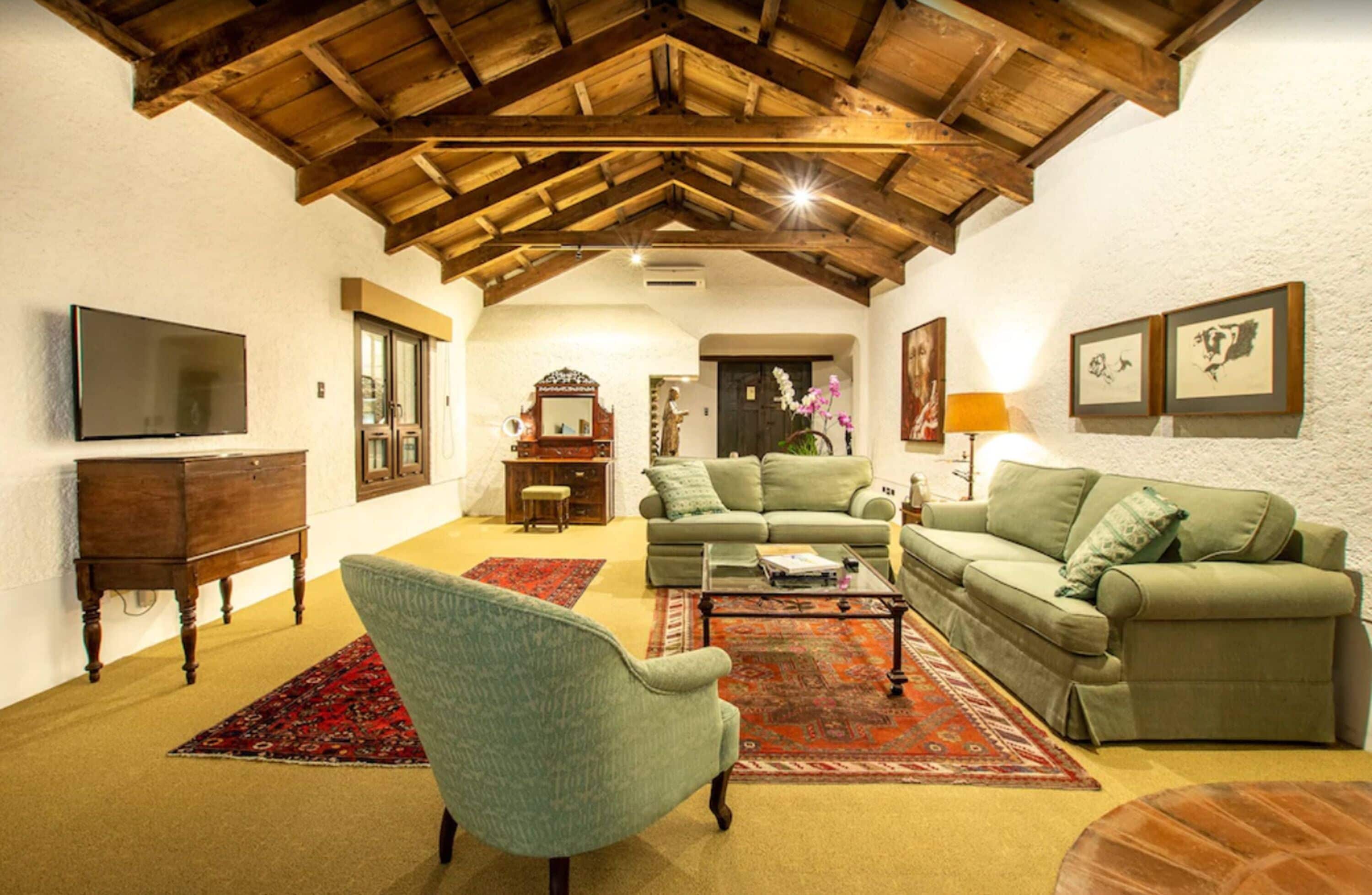 Un soggiorno con soffitto in legno, divani verdi, una televisione e un caminetto.