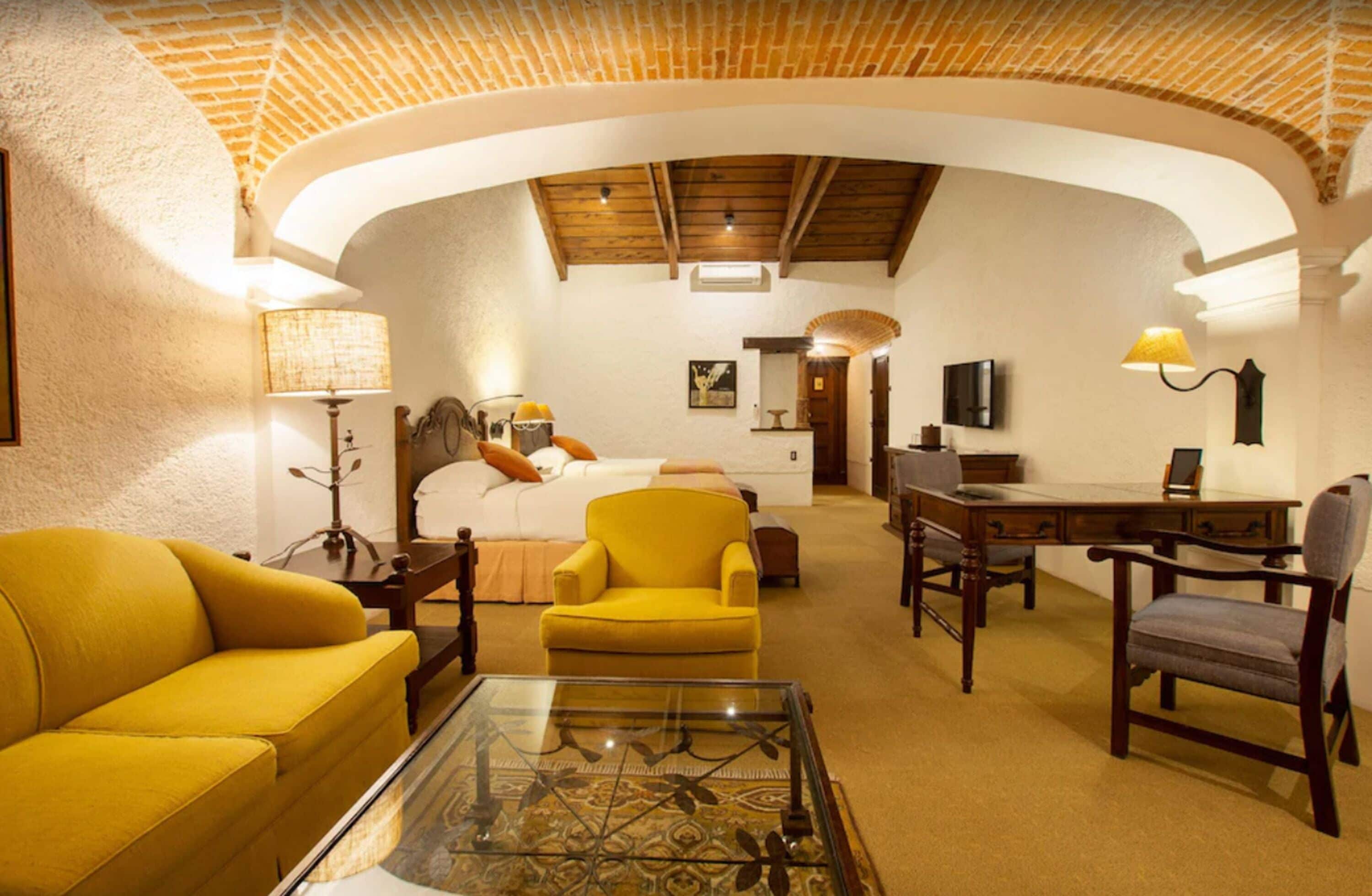 A spacious room with a high arched ceiling, a bed, a desk, and a yellow armchair.