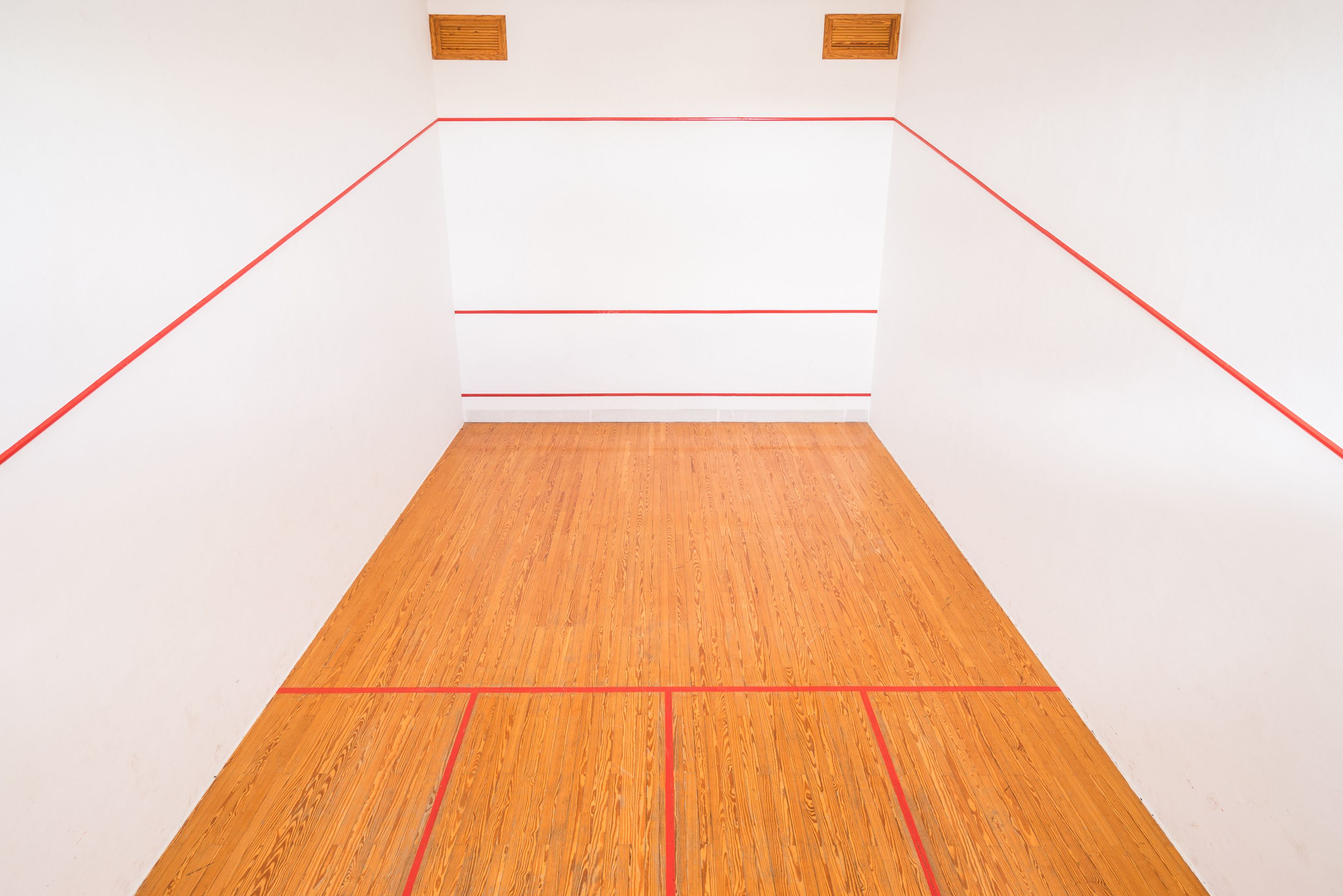 Una cancha de squash con suelo de madera y líneas de demarcación rojas.