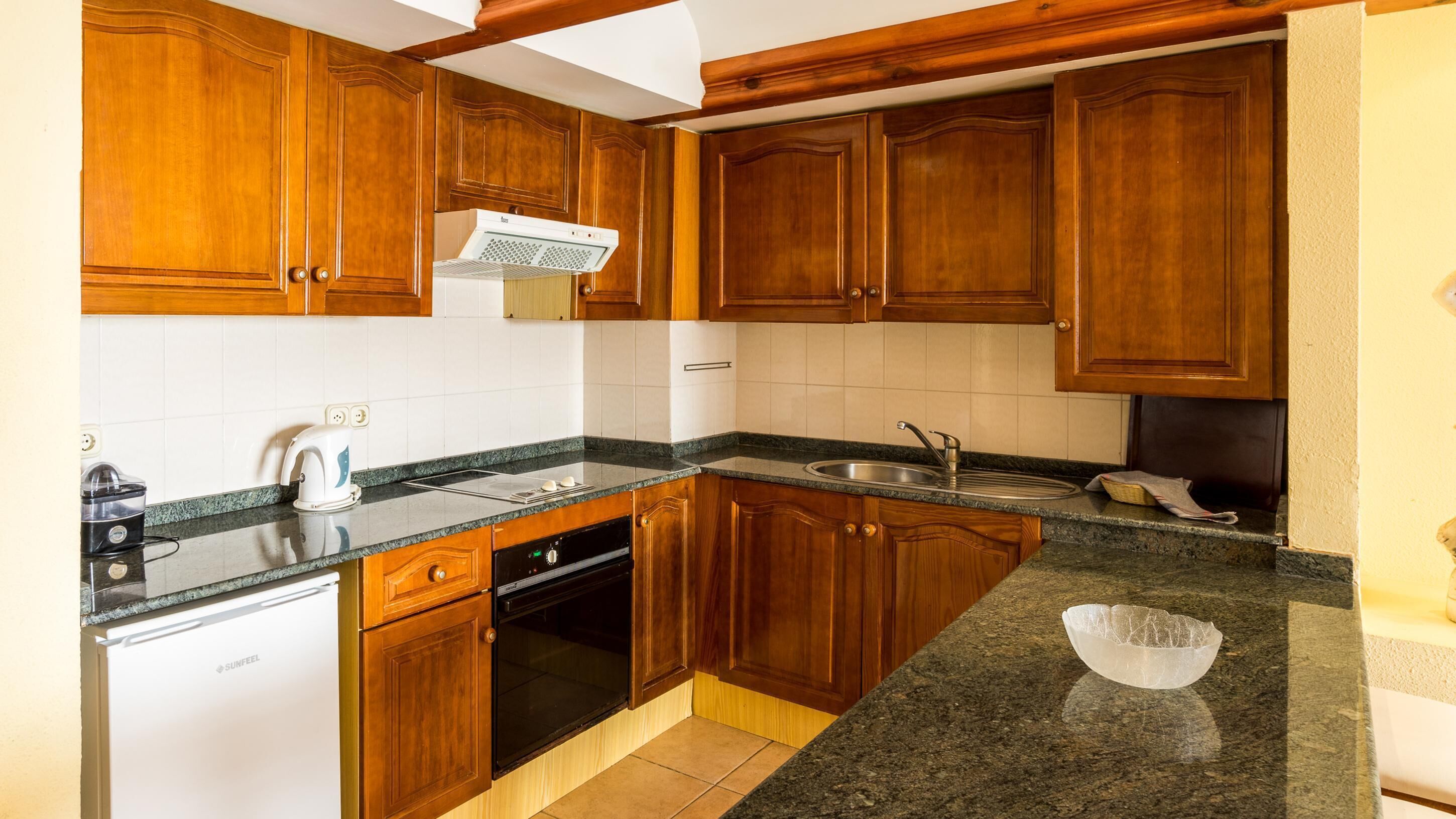 Una cocina con armarios de madera, horno empotrado, lavavajillas y encimera de granito.