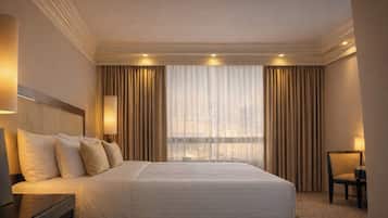 Een hotelkamer met een groot bed, twee bedlampen, een stoel en uitzicht op de stad door dunne gordijnen.