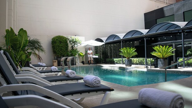 A poolside area with lounge chairs and towels, surrounded by greenery and a modern building facade. - Regal Pacific Buenos Aires (Buenos Aires)