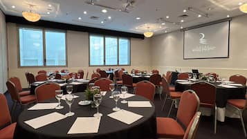A conference room with round tables, red chairs, and a projector screen displaying the hotel name.