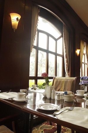 A dining area with a table set for two, a vase with a single flower, and a view of greenery outside through a large window. - Homeland Hotel (Chengdu)