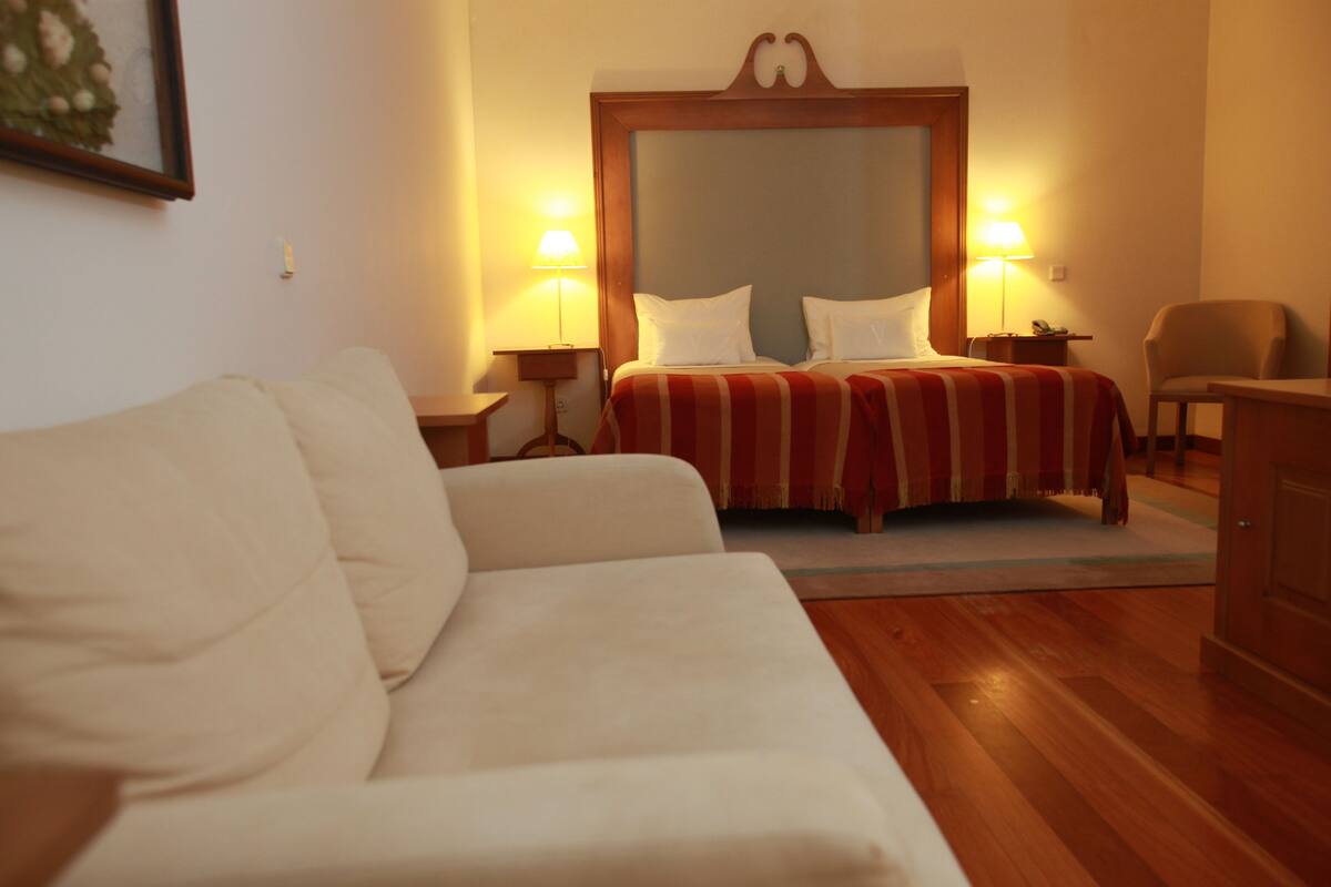 Een hotelkamer met een bed, een slaapbank, een houten vloer en twee bedlampen.