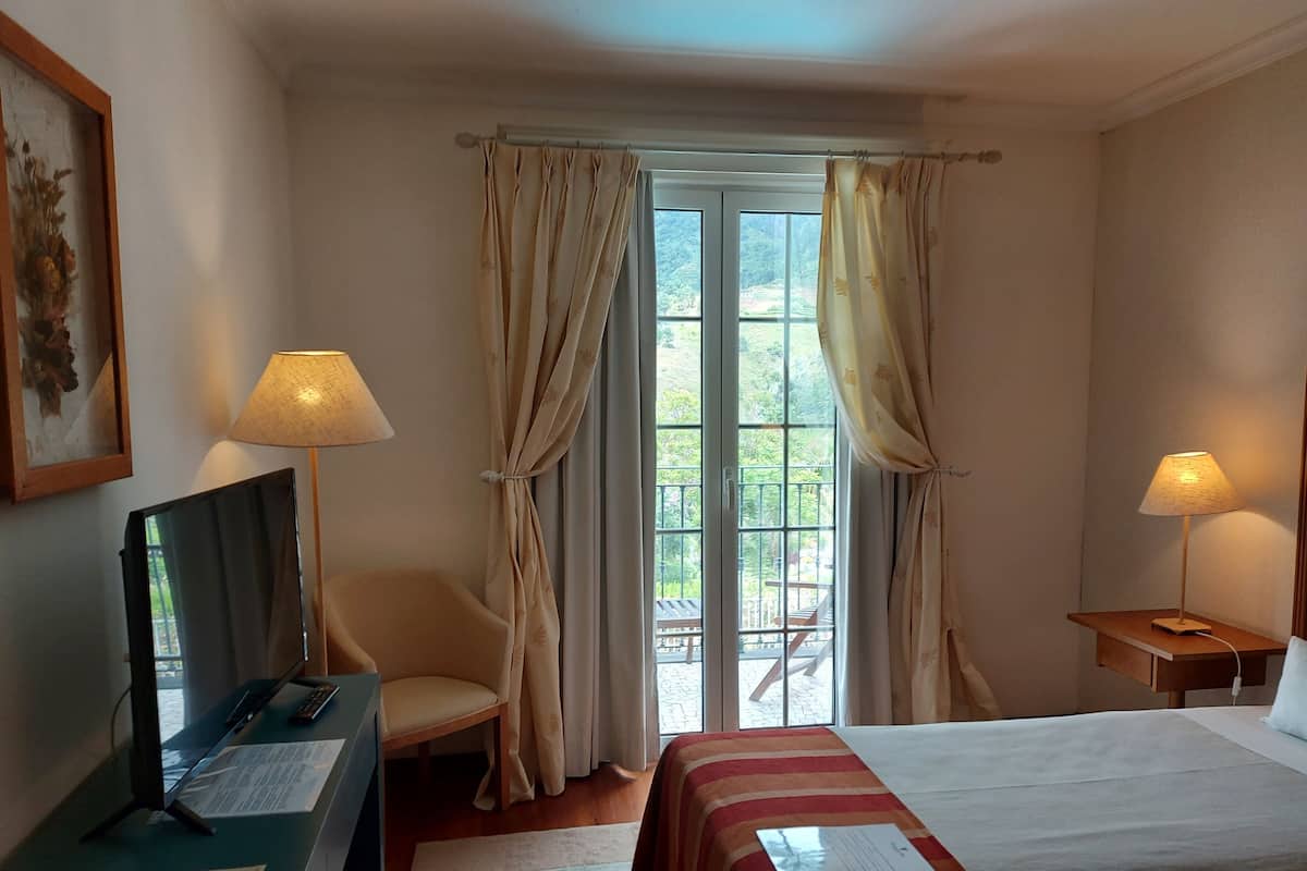 Hotelkamer met een bed, een bureau met een computer, een stoel, een bureaulamp en een raam met gordijnen.