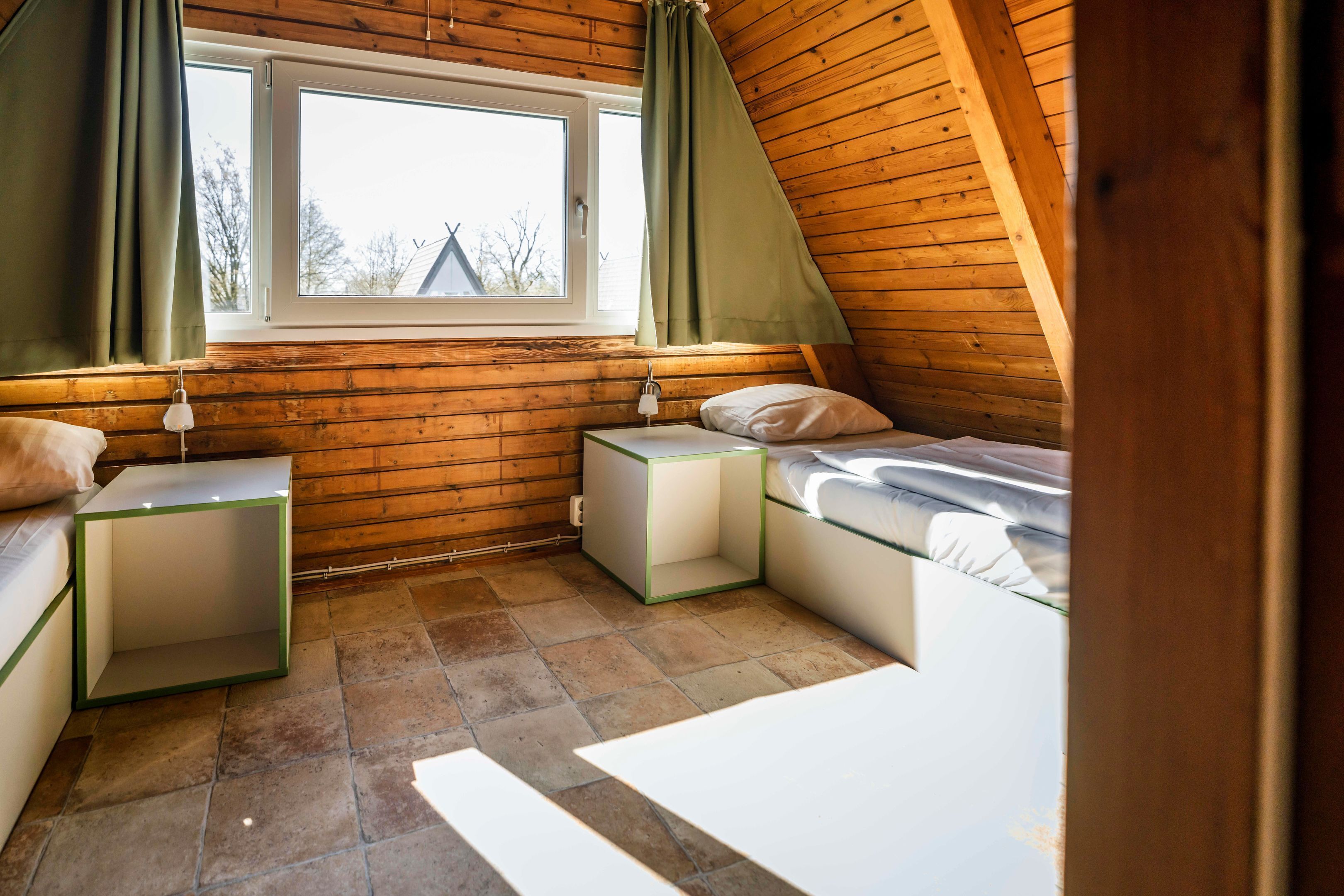 Ein gemütliches Schlafzimmer im Dachgeschoss mit schrägen Wänden, einem Fenster mit Vorhängen, einem Bett, einem Nachttisch und einem kleinen Tisch.