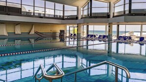 Una piscina interna con acqua cristallina, diverse corsie e sedie a sdraio rivolte verso l'oceano.