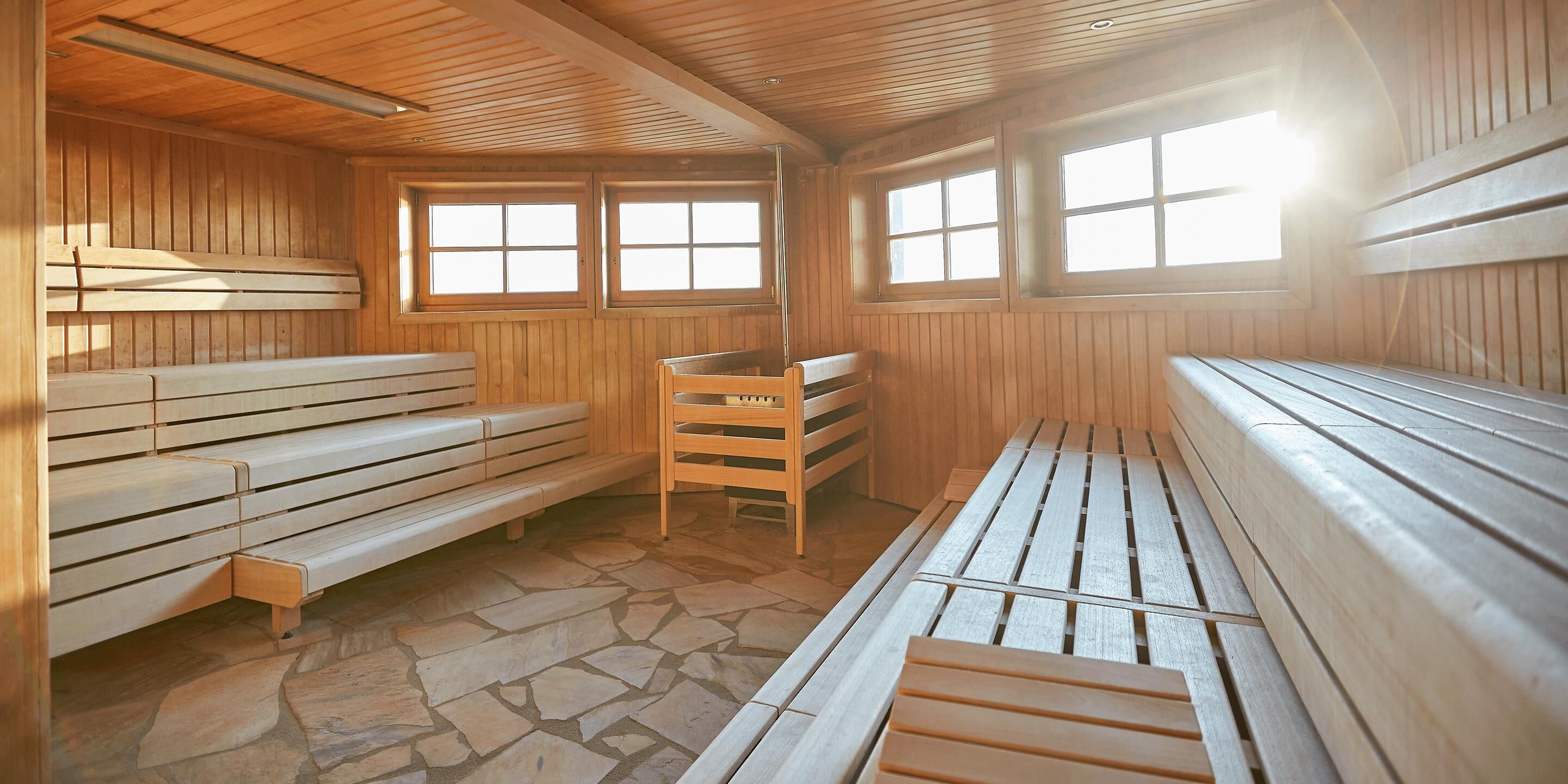 Un sauna avec des bancs en bois, un sol en pierre et de grandes fenêtres qui laissent entrer la lumière naturelle.