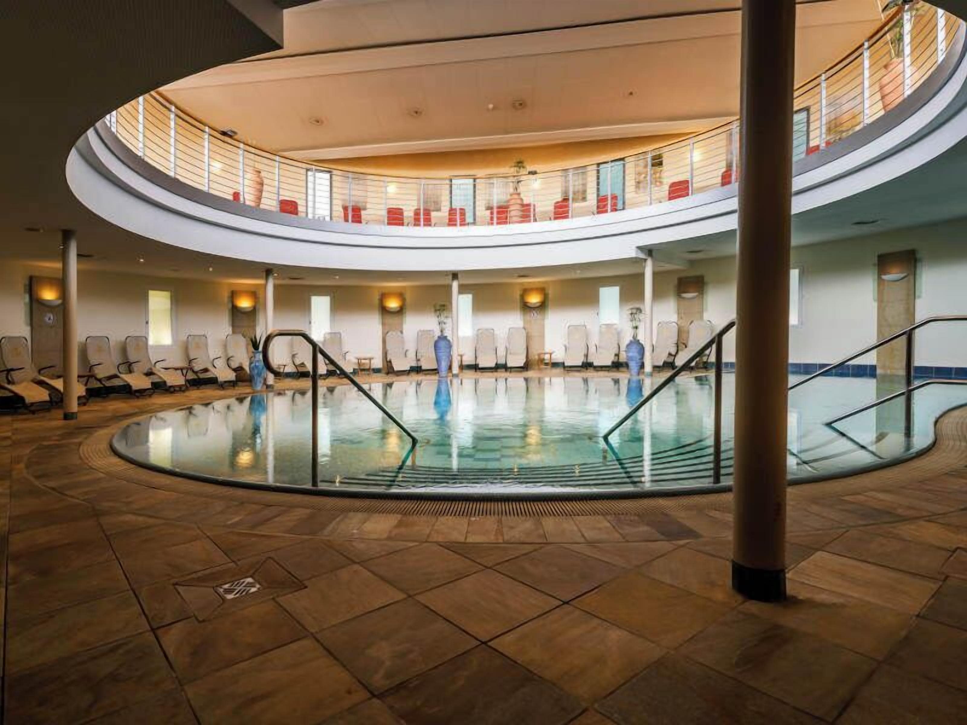 A multi-level indoor swimming pool with a glass floor, multiple seating areas, and a central staircase.