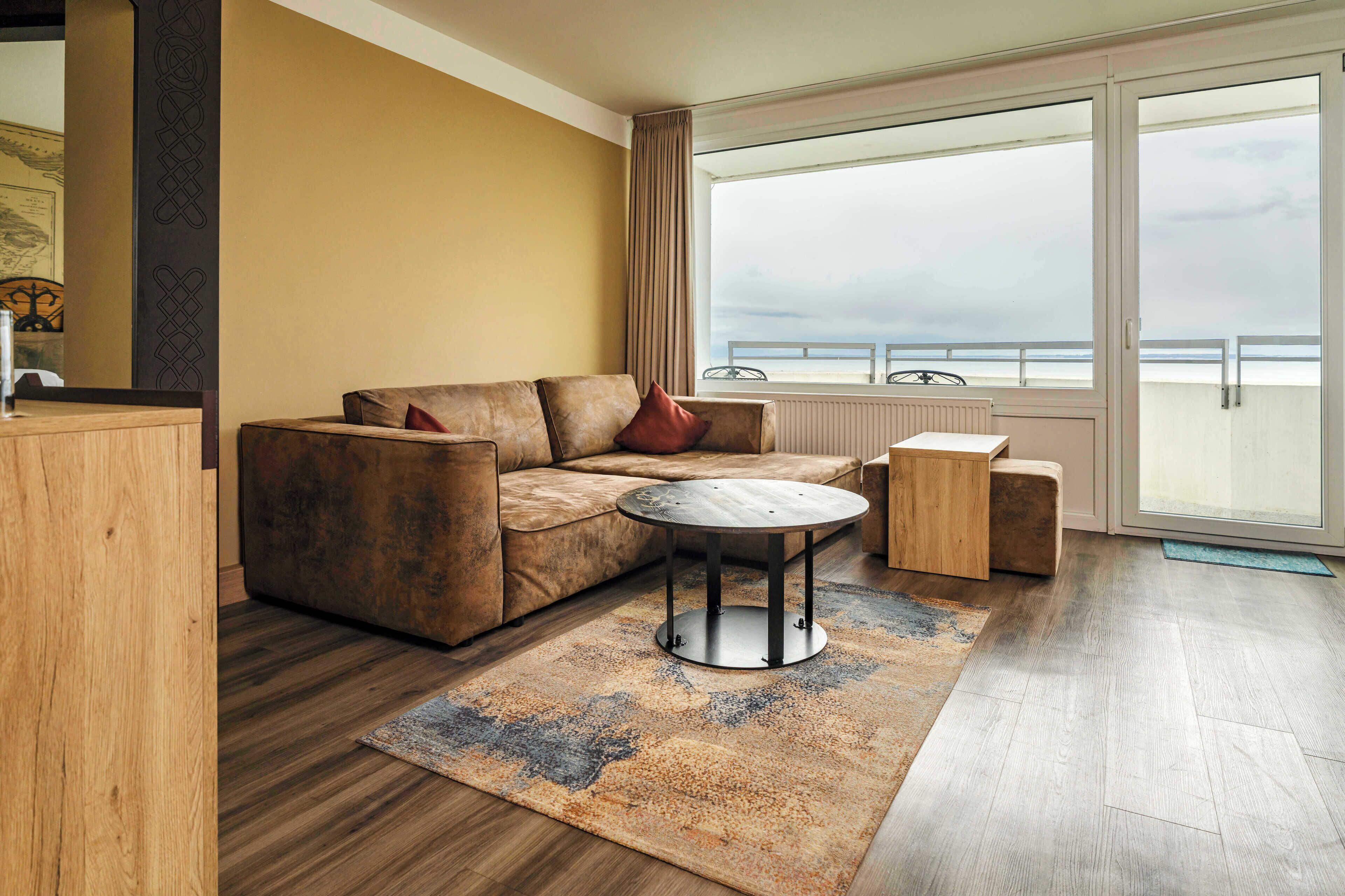 Ein modernes Wohnzimmer mit Sofa, Couchtisch und Beistelltisch. Ein großes Fenster bietet Blick auf das Meer.