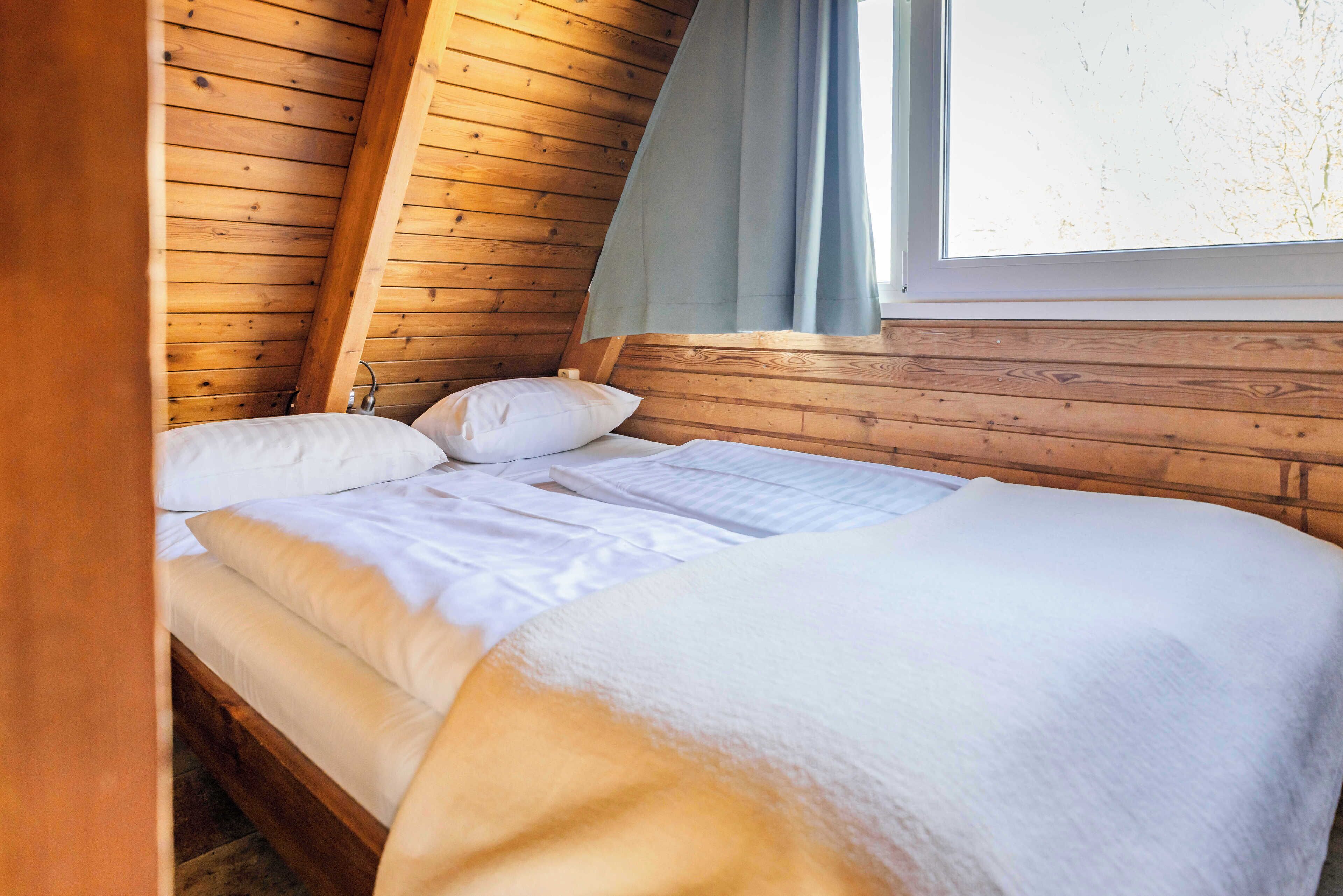 Ein Schlafzimmer einer Holzhütte mit Bett, Kissen und einem Fenster mit Vorhängen.