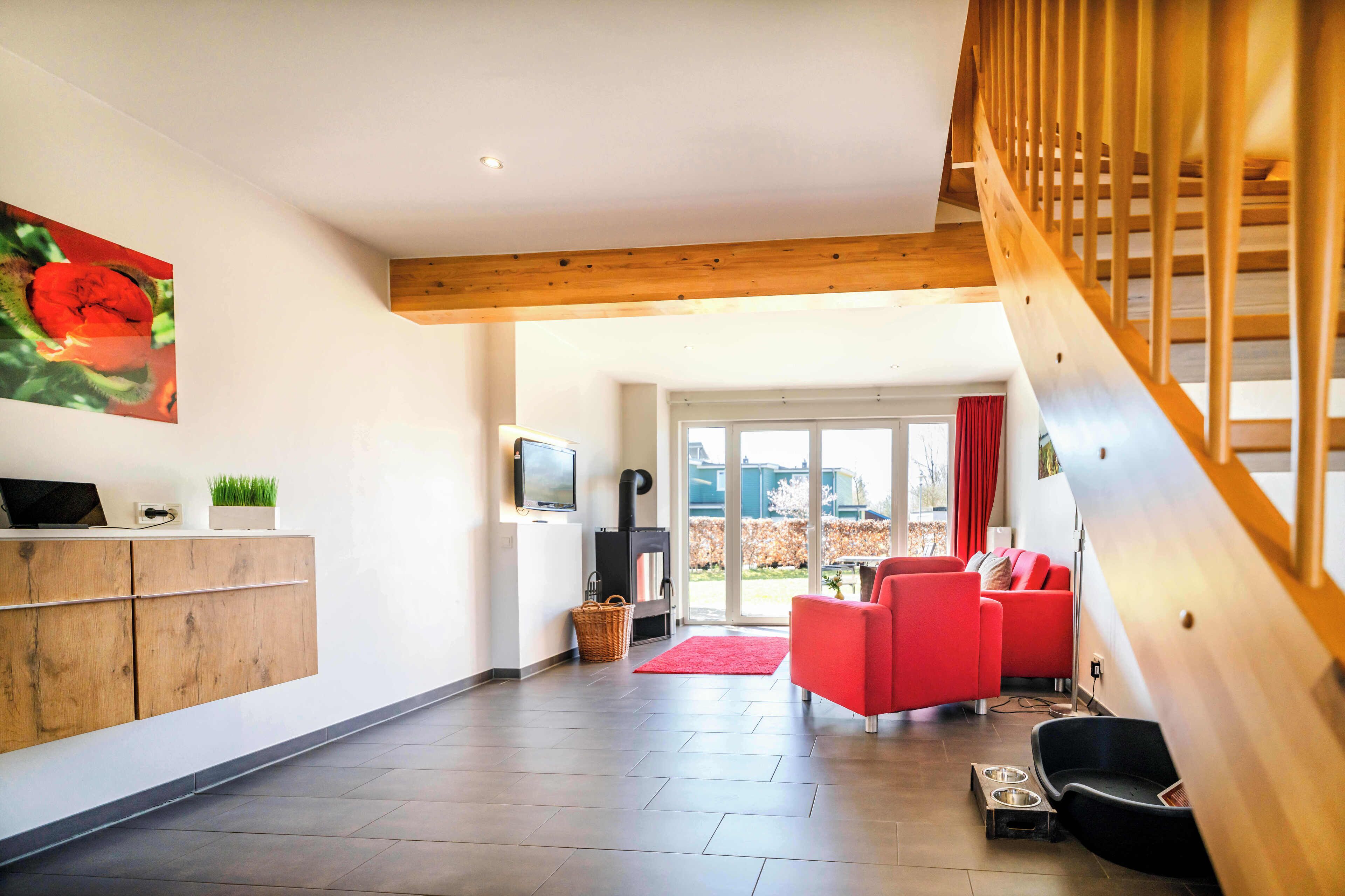 A modern living room with a wooden staircase, a red sofa, and a fireplace.