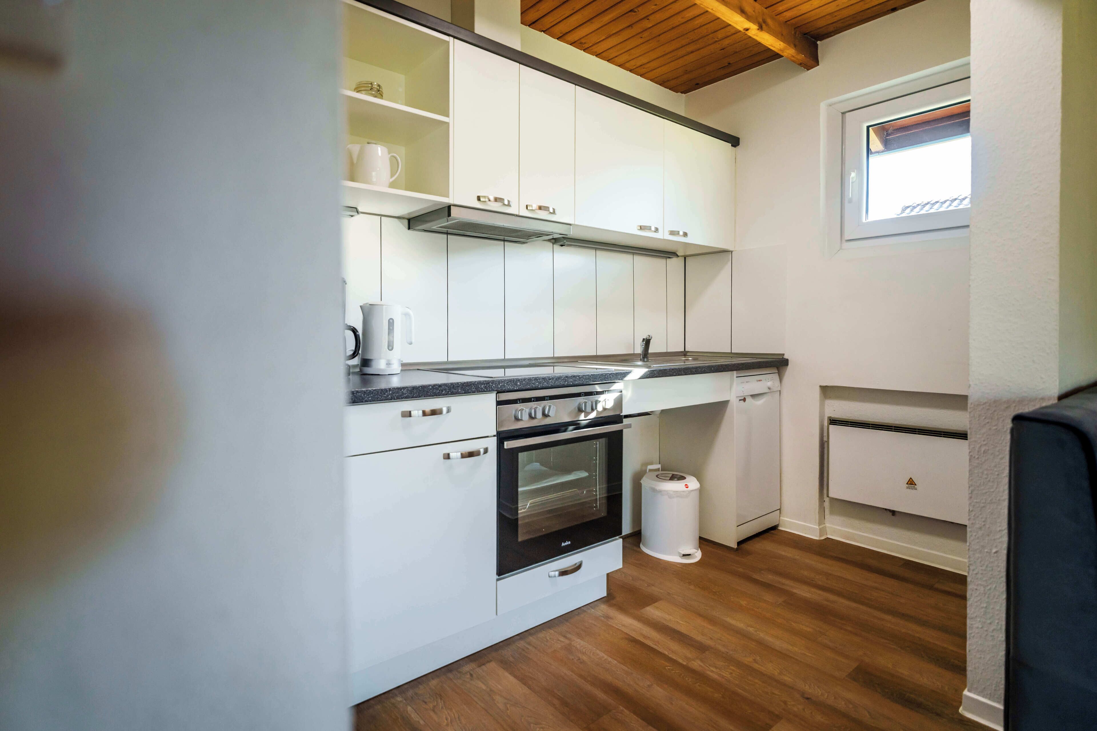 A compact kitchen with white cabinets, a built-in oven, a coffee maker, and a window.