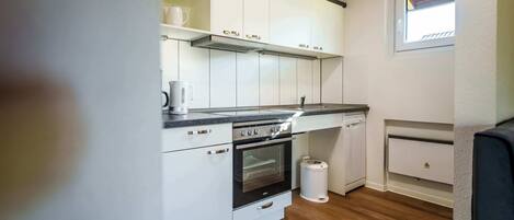 A compact kitchen with white cabinets, a built-in oven, a coffee maker, and a window.