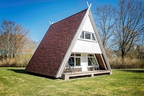 Ein modernes, dreieckiges Haus mit geneigtem Dach, großen Fenstern und einer Holzterrasse.