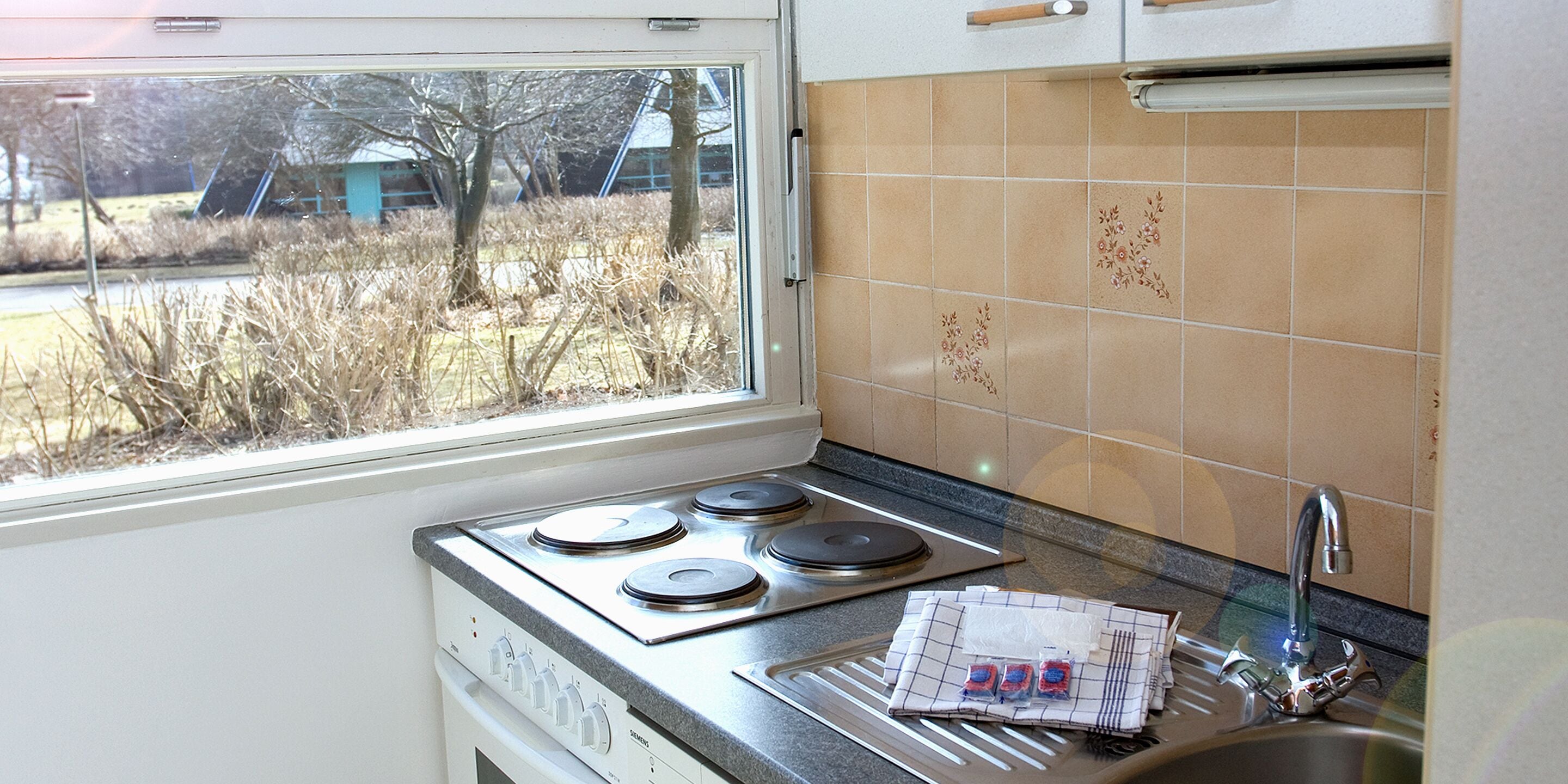 Una cocina con estufa, lavamanos y ventana con vista a un área verde.