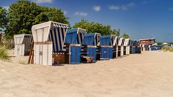 A row of beach huts with striped awnings, arranged on a sandy beach with trees in the background.