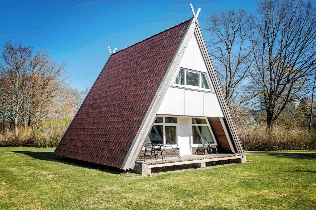 Un edificio moderno de forma triangular, con techo inclinado, ventanas amplias y una terraza de madera.