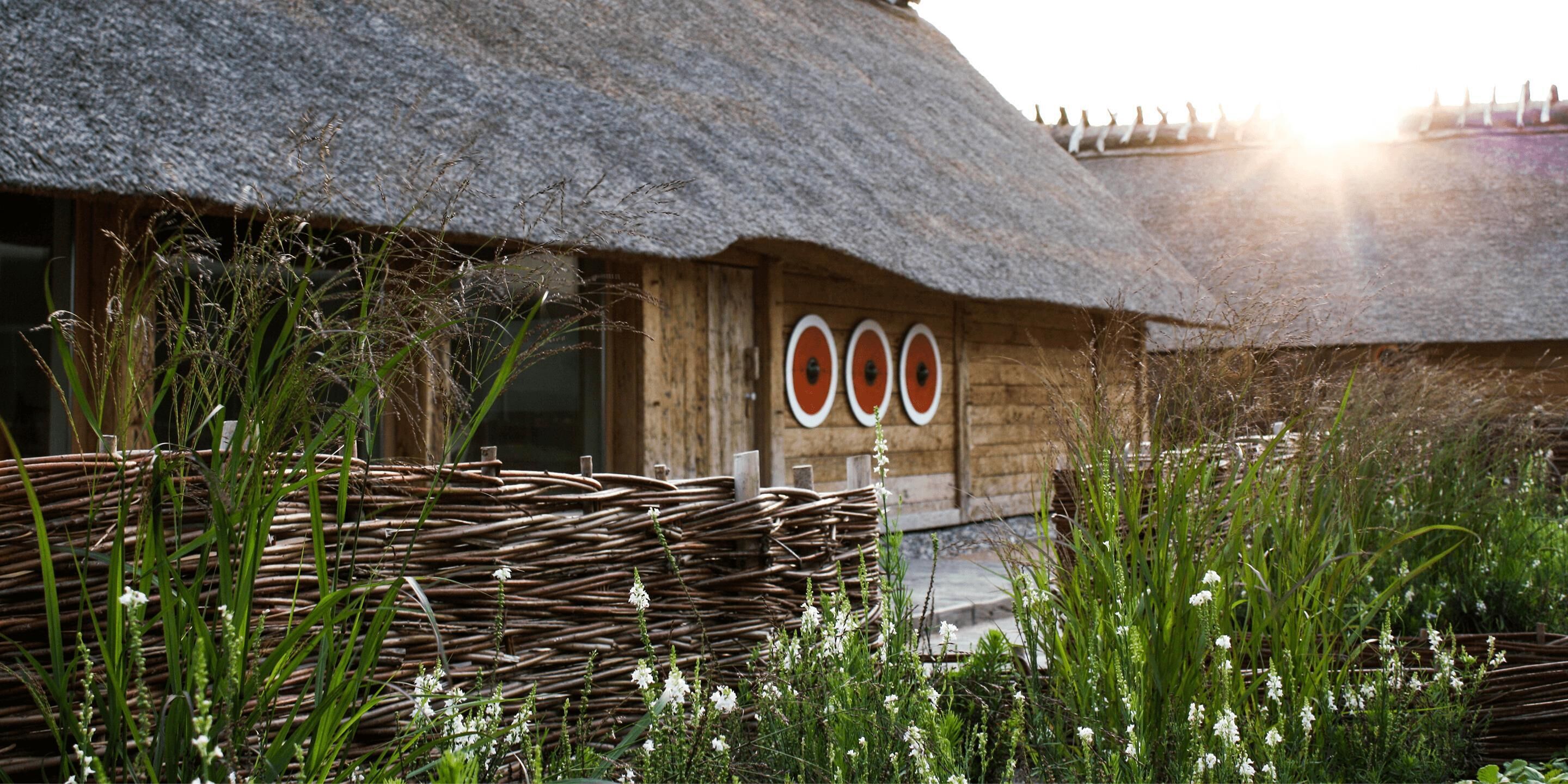 A thatched-roof building with a woven basket in the foreground and a wooden door with circular windows.