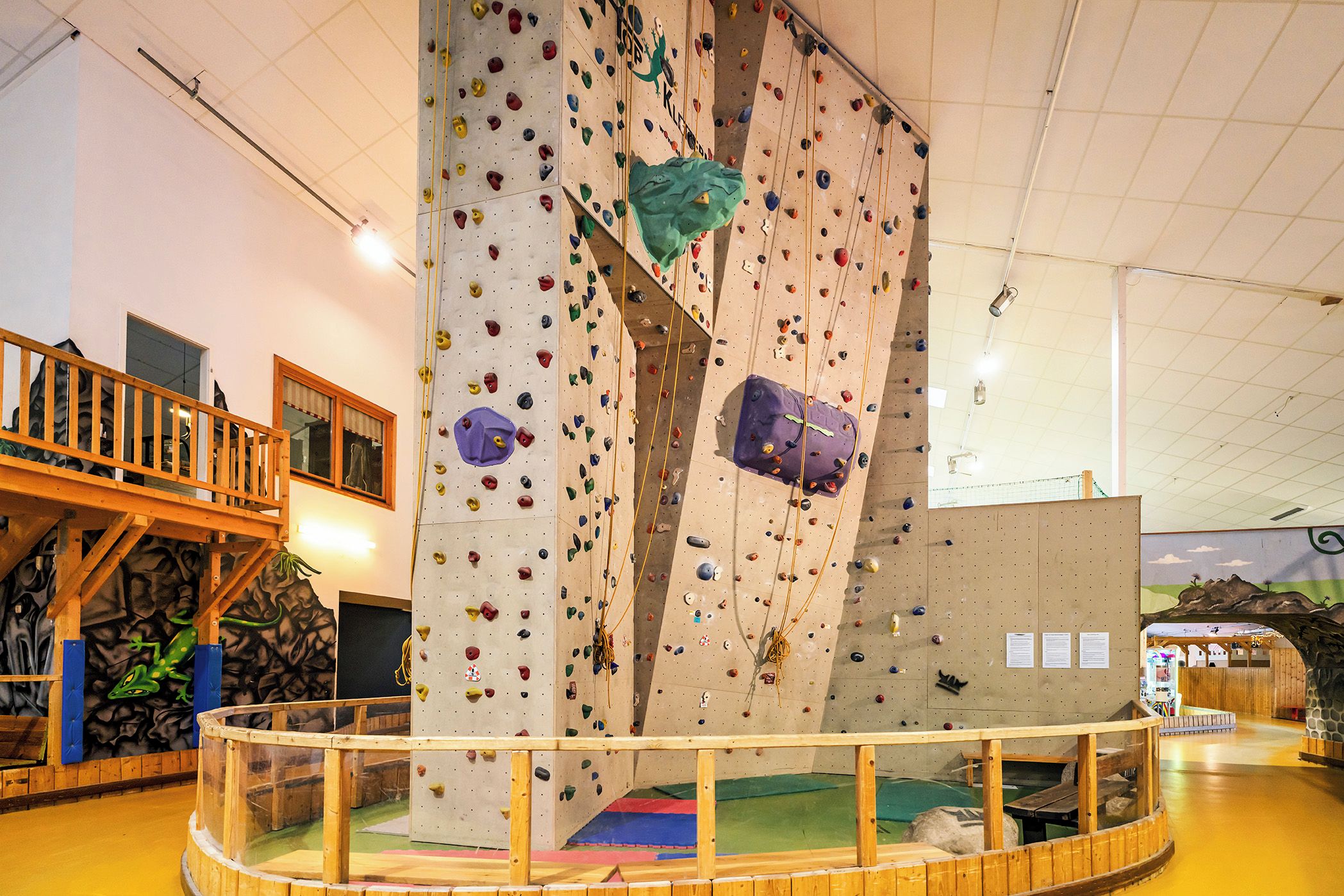 An indoor climbing wall with various holds and a wooden viewing platform.