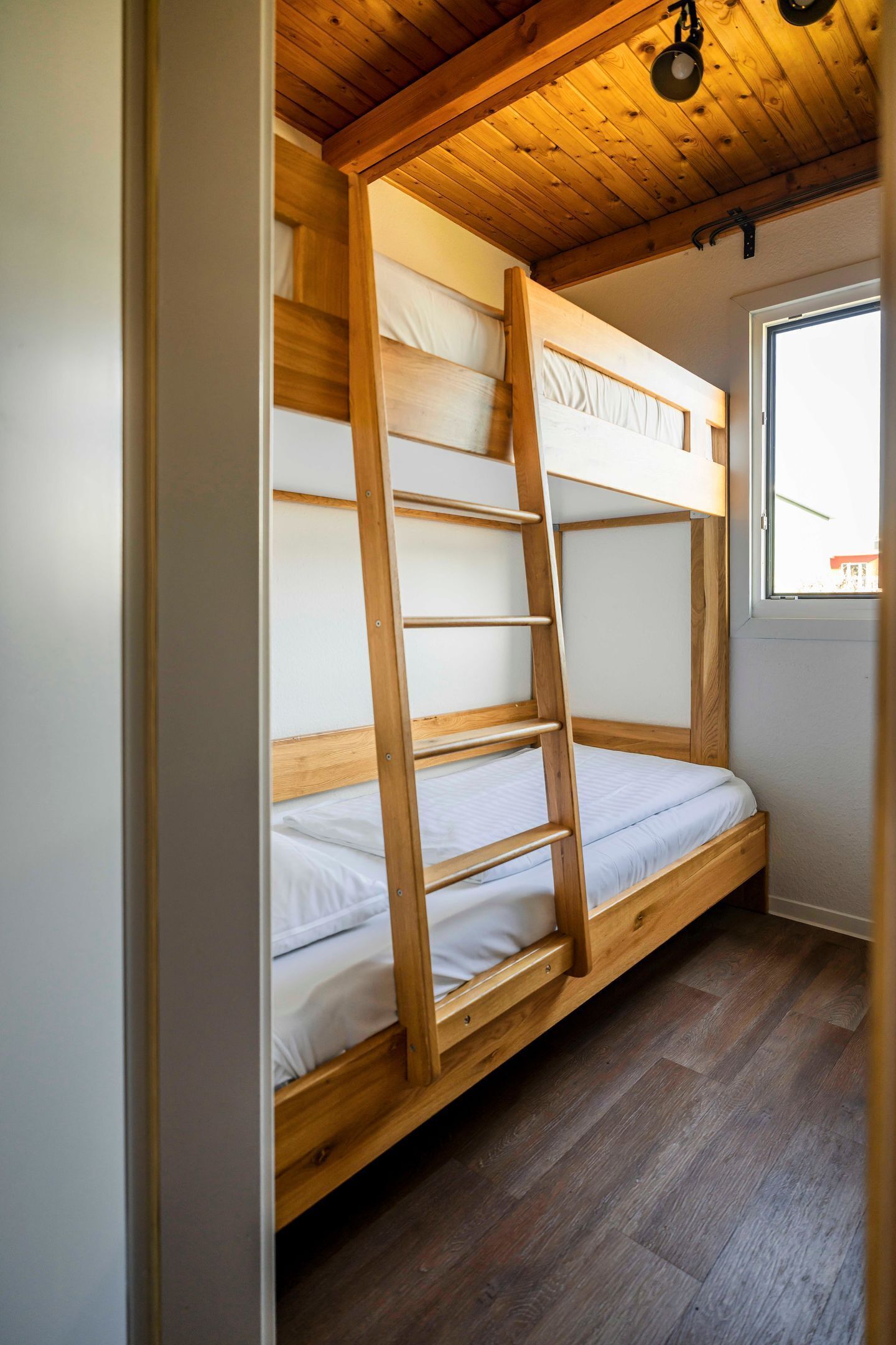 Una cama litera con escalera de madera, ventana con vistas y suelo de madera.