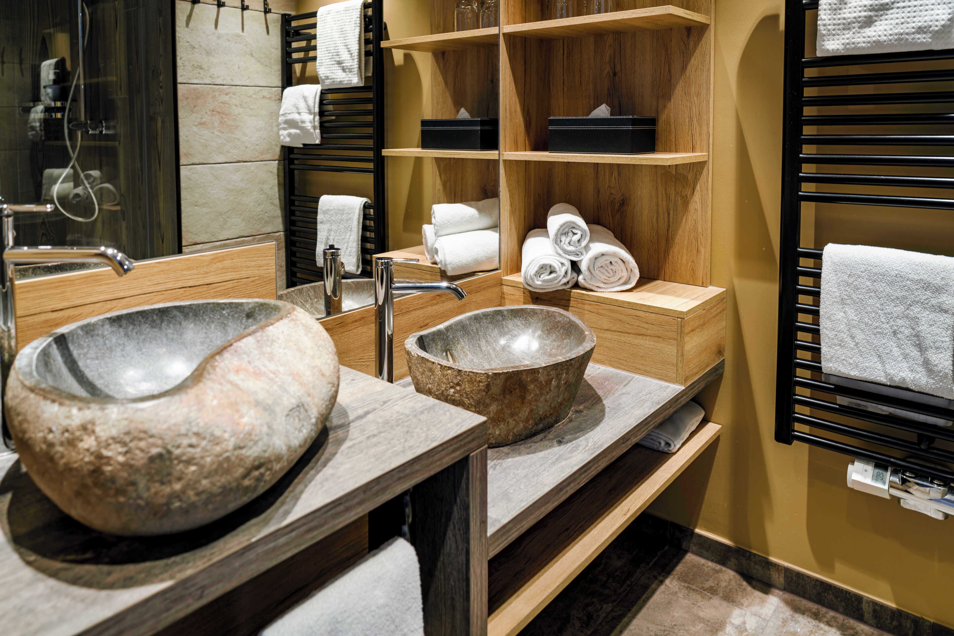 A bathroom with a large stone sink, wooden shelves, and a black towel rack.