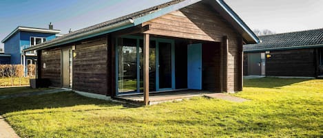 Una casa moderna con fachada de madera, puertas de cristal amplias y un porche cubierto.