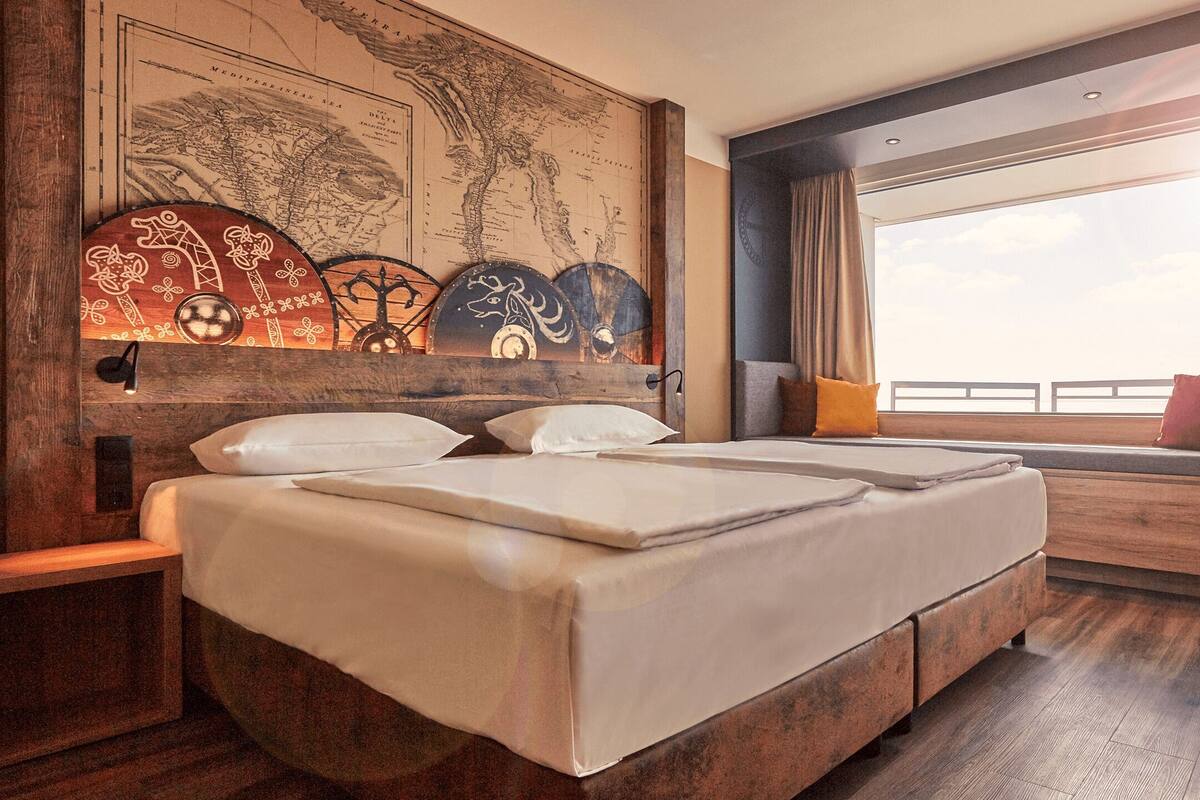 Habitación de hotel con una cama grande, un escritorio, vista al mar y un mapa mundial en la pared.