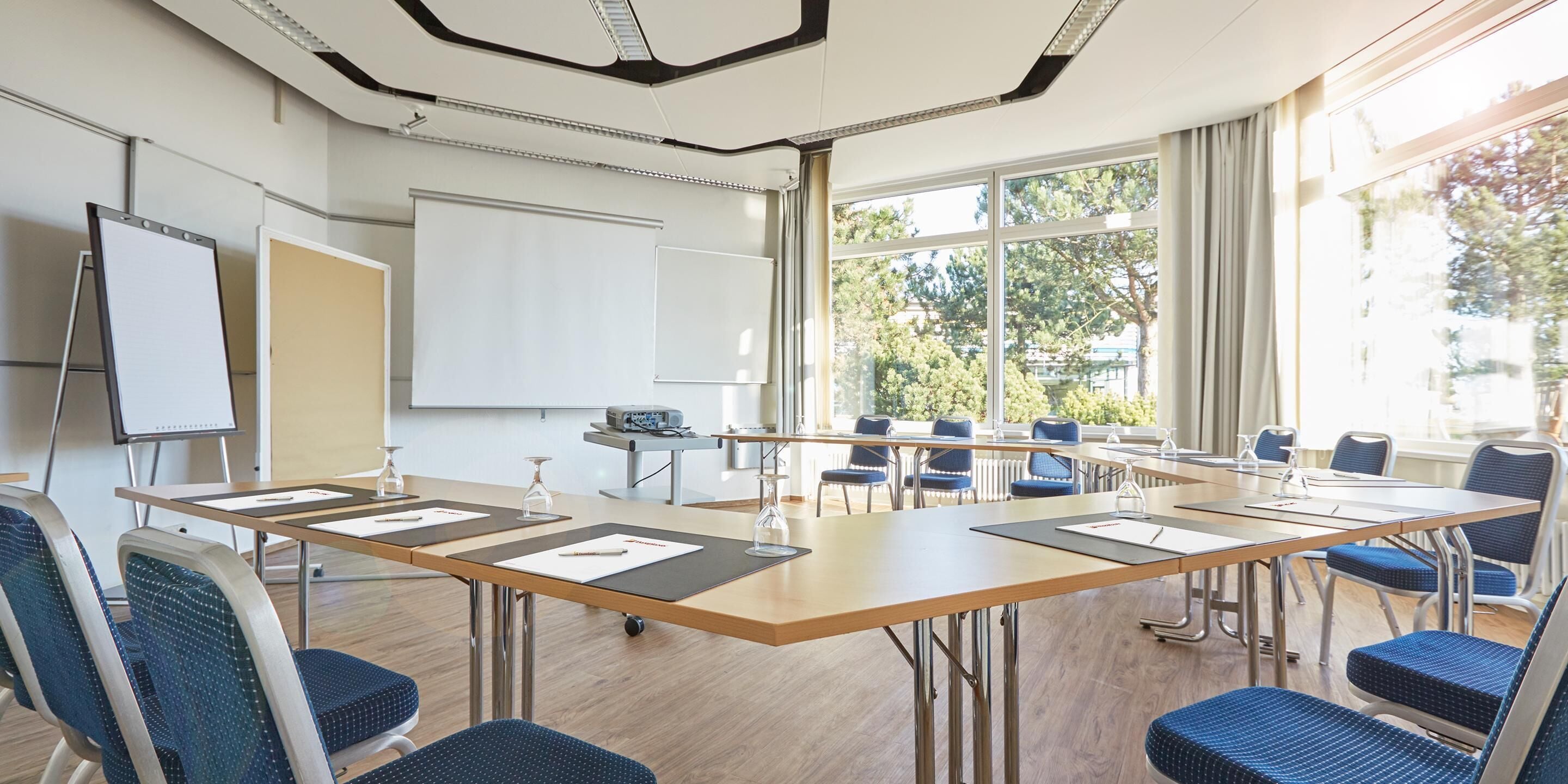 Een vergaderzaal met een grote tafel, stoelen, een whiteboard en een beamer.