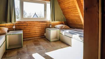 A cozy attic bedroom with a sloped ceiling, a window with curtains, a bed, bedside tables, and a small table.