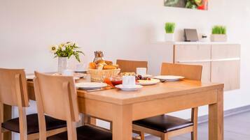 A wooden dining table with four chairs, a vase of flowers, a basket of bread, and a coffee cup.