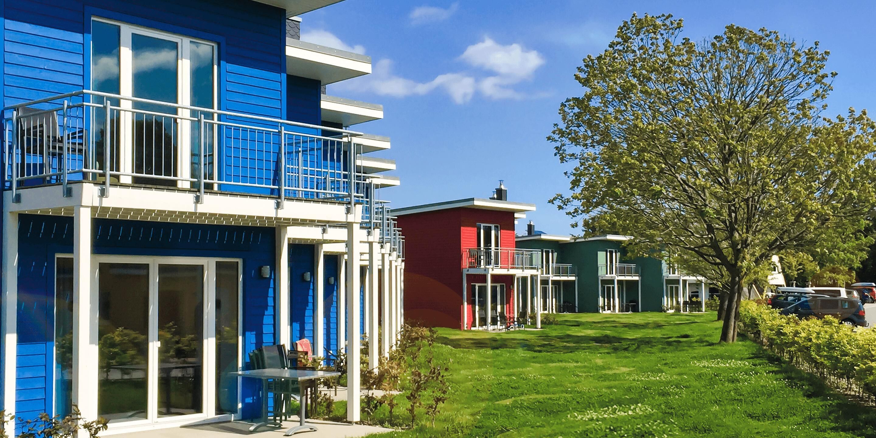 Ein modernes Gebäude mit blau-roter Fassade, einem Balkon und einer grünen Rasenfläche.