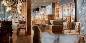 Ein Restaurantinneres mit Holztischen, hängenden Lampen und einer Steinwand.