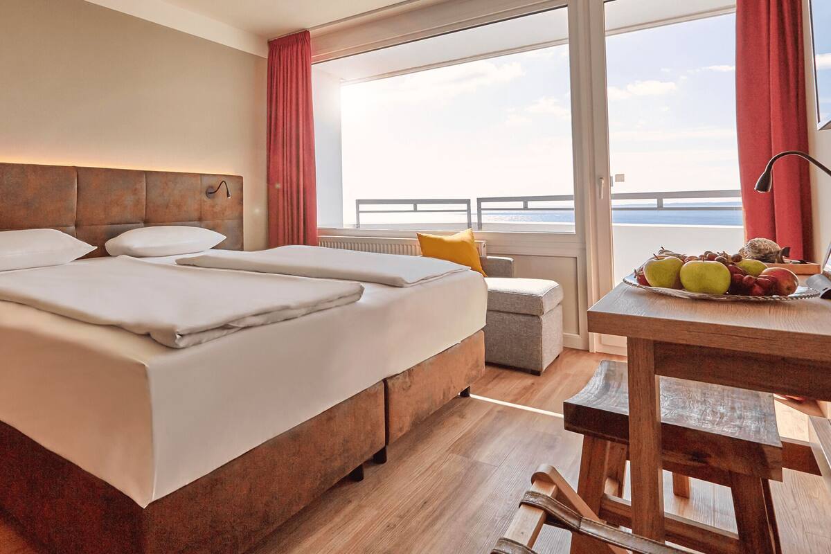 Una habitación de hotel con una cama grande, una mesita con fruta y vistas al mar.