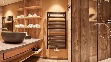 A modern bathroom with a large bathtub, wooden shelves with towels, and a walk-in shower.