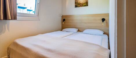 Un lit double avec une tête de lit en bois, une fenêtre avec des rideaux et un luminaire fixé au mur.