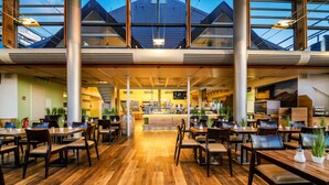 Un ristorante spazioso con soffitti alti, pavimento in legno e ampie finestre. Tavoli e sedie disposti per la ristorazione.