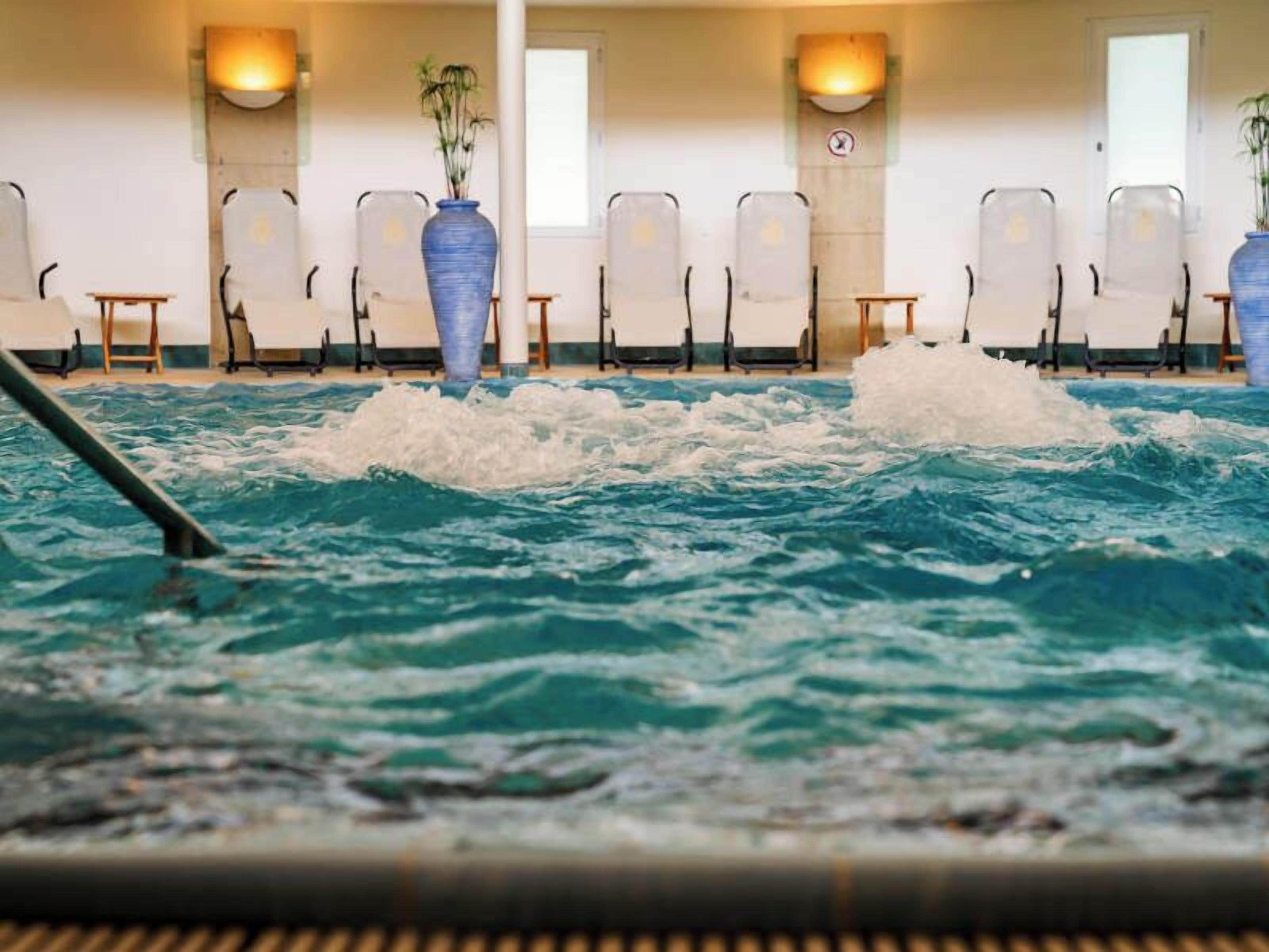 An indoor swimming pool with clear water, surrounded by lounge chairs and potted plants.