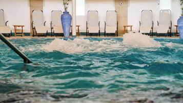 An indoor swimming pool with clear water, surrounded by lounge chairs and potted plants.