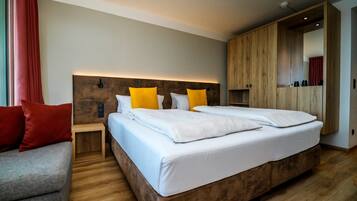 Ein modernes Hotelzimmer mit einem großen Bett, einem Holzkopfstück, einem kleinen Nachttisch, einem grauen Sofa und einem Kleiderschrank.
