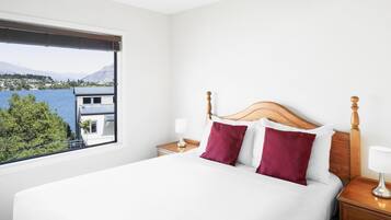 Een hotelkamer met een bed, twee nachtkastjes, een raam met uitzicht op een berg en gebouwen, en een uitzicht op een meer.