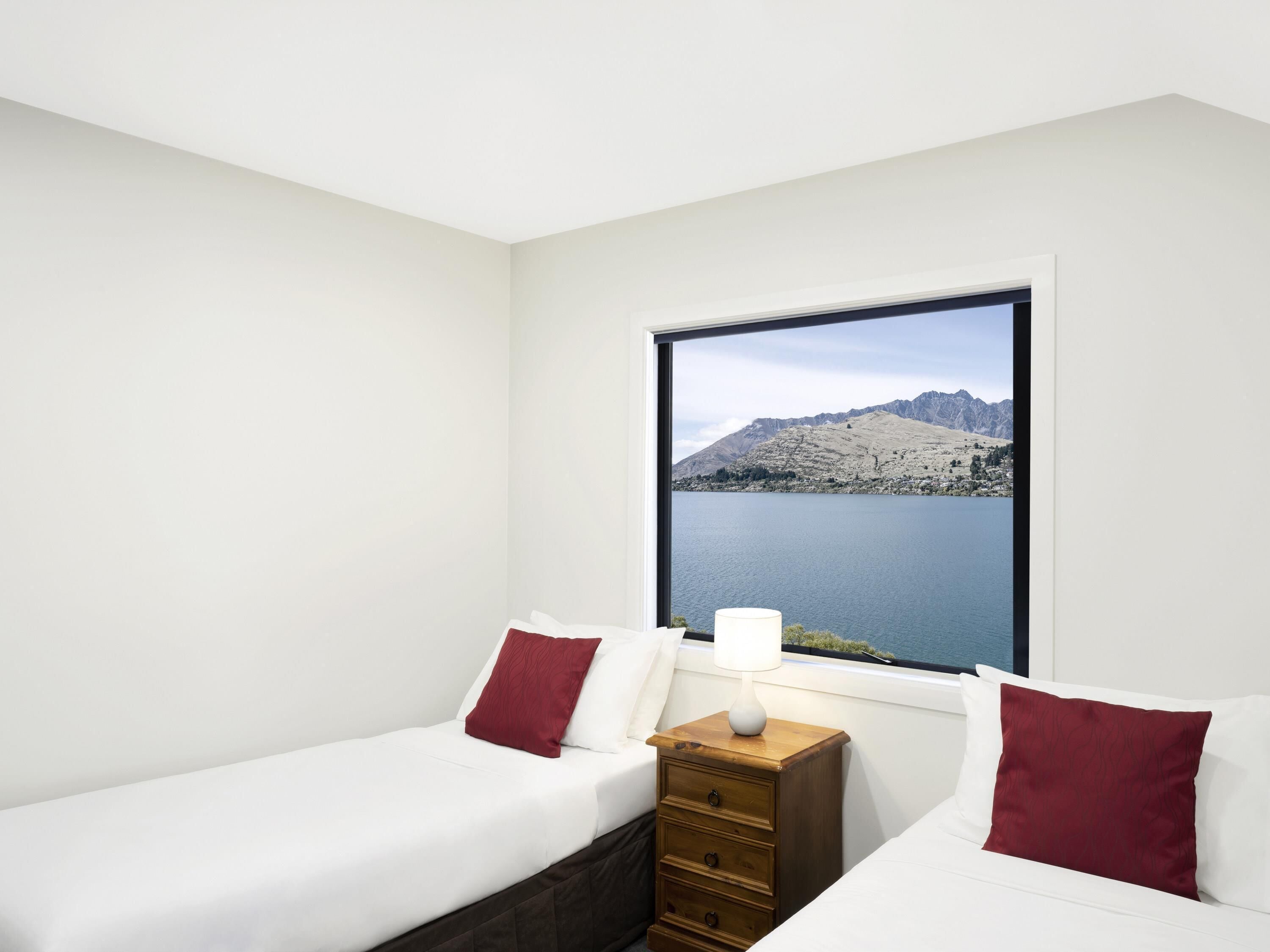 Ein Schlafzimmer mit zwei Betten, einem Nachttisch mit Lampe und einem Fenster mit Blick auf die Berge.