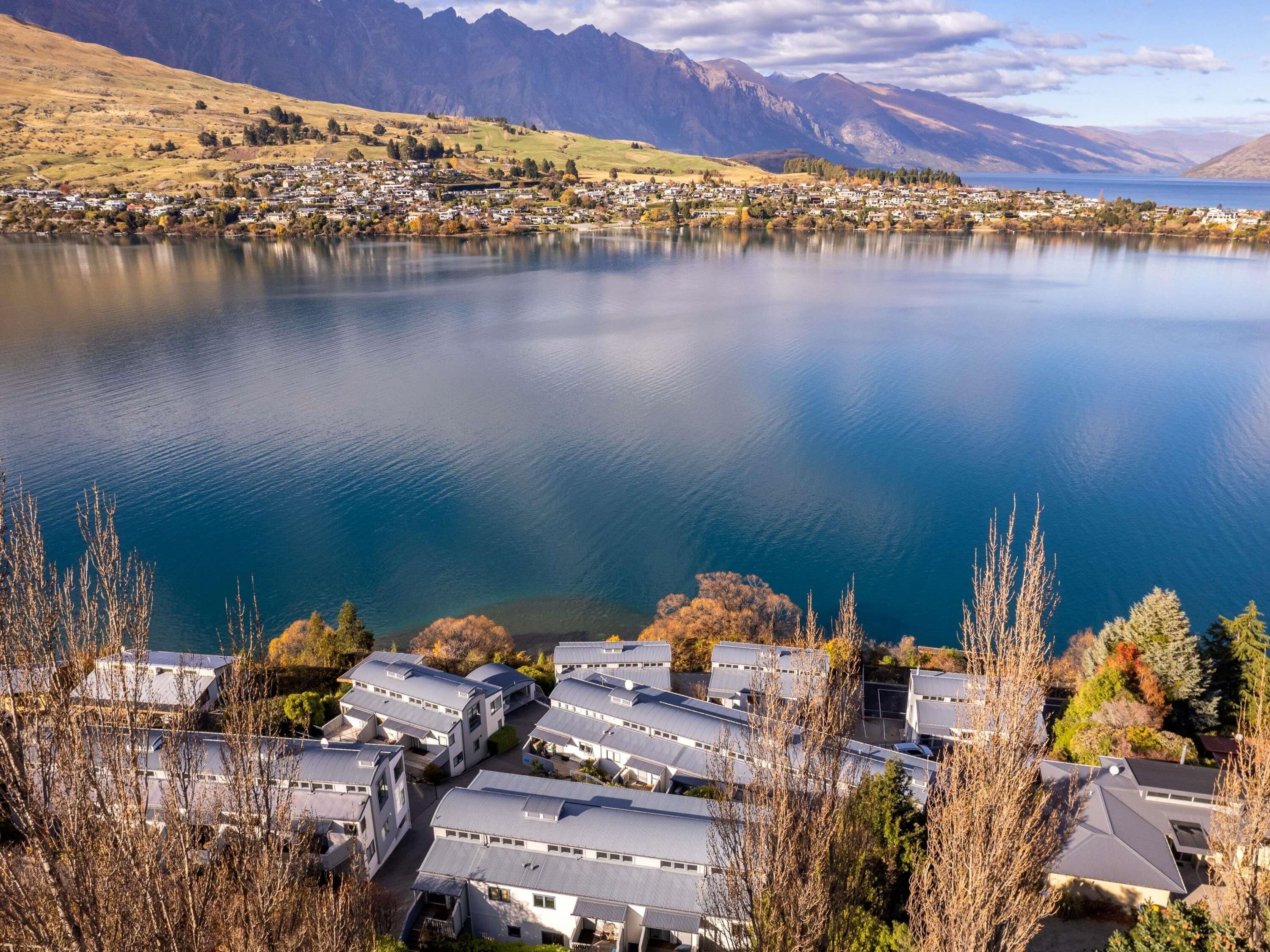 A lakeside residential area with modern houses, a clear view of the lake, and mountains in the background.
