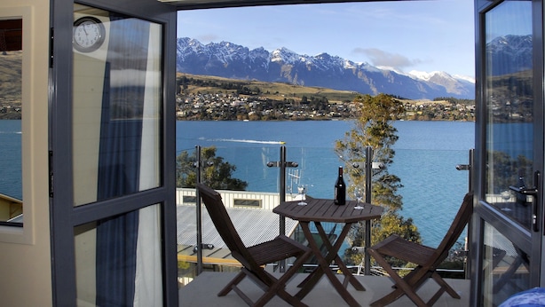 Ein Balkon mit einem Holztisch und zwei Stühlen, mit Blick auf einen See und Berge.