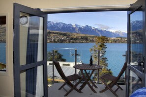 Un balcón con una mesa de madera y dos sillas, con vista a un lago y montañas.