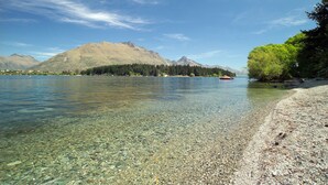 Ein klarer See mit kiesigem Ufer, umgeben von Bergen und Bäumen.