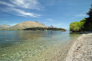 A clear lake with a pebbly shore, surrounded by mountains and trees.